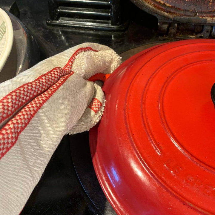 Gauntlet long oven glove linen union with red stripes  holding a red cast iron pot handle on the Aga  cooking ring