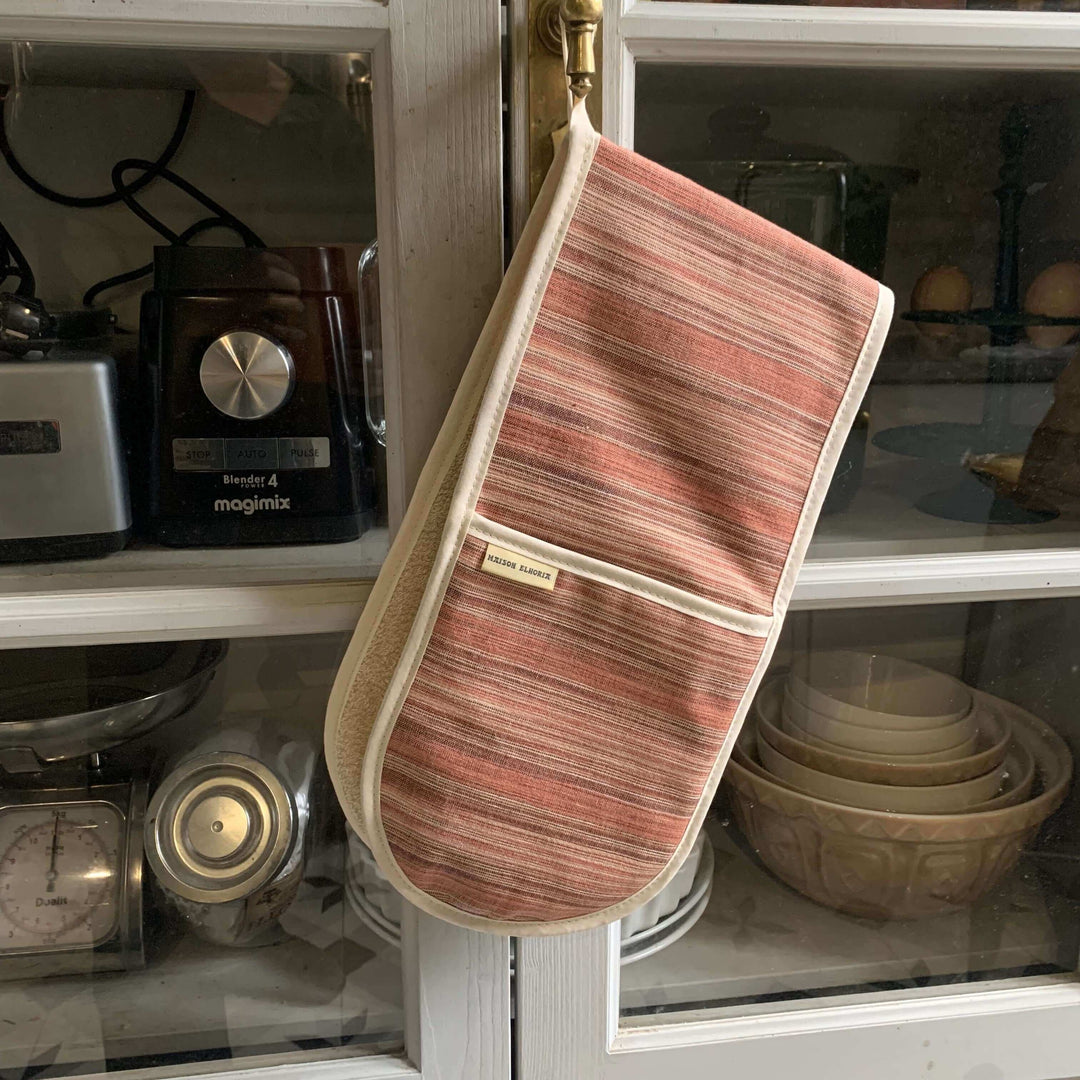  Red oven mitts double handed, hanging off a kitchen wooden and glass cupboard 