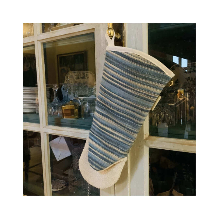 long gauntlet style oven mitt with blue vertical stripes hanging off a kitchen cupboard door