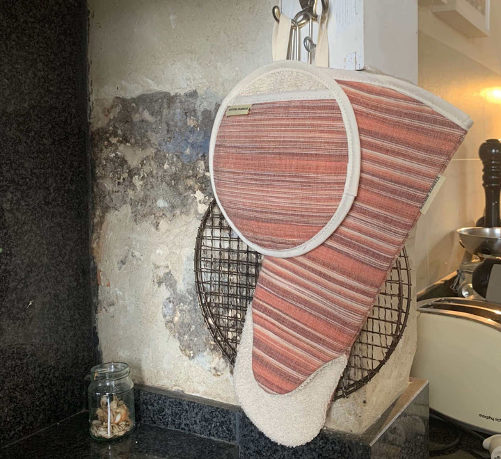 one pot holder round shaped and one gauntlet style matching red striped oven gloves hanging off an old kitchen wall, close up photo
