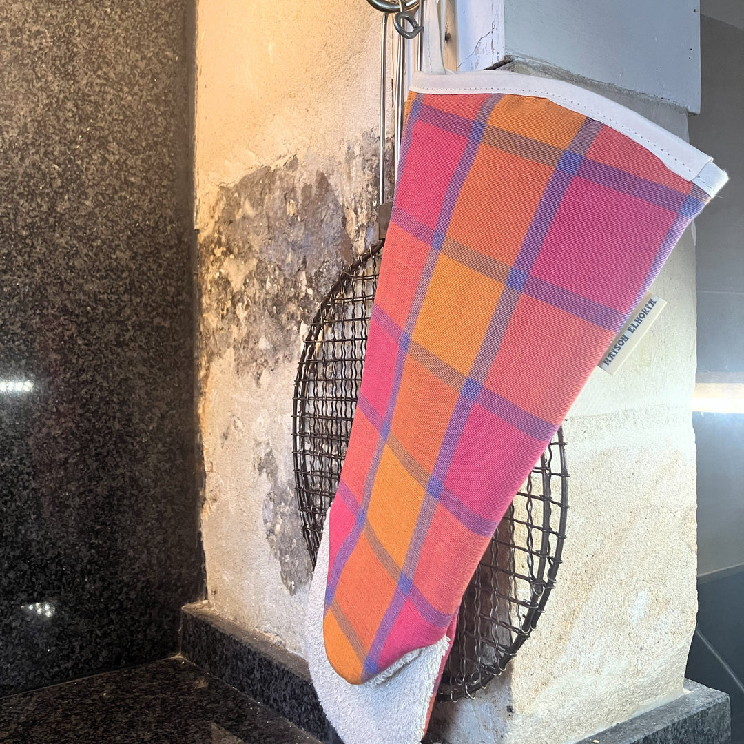 Plaid oven mitt orange pink and blue hanging in a rustic kitchen with an Aga bread toasting utensil in the background 
