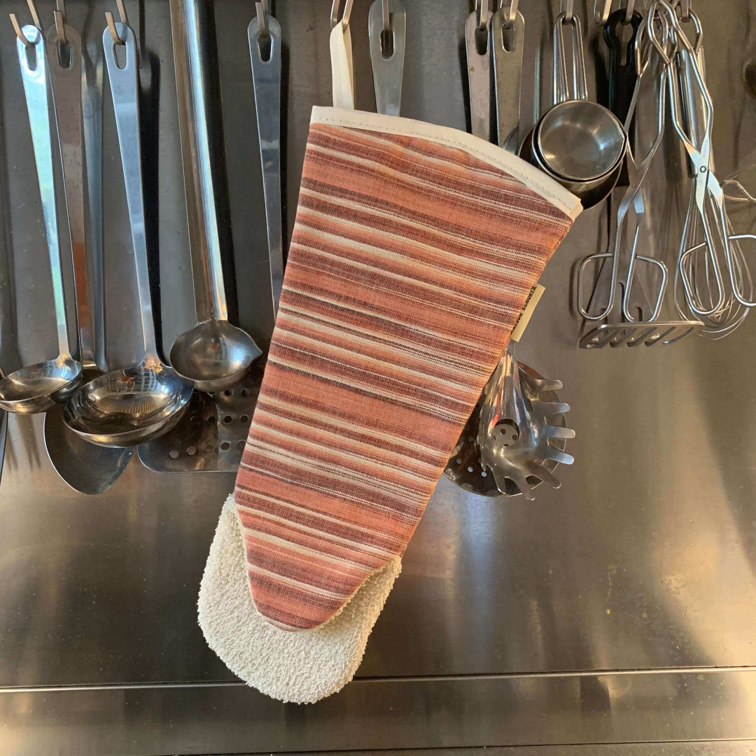 Oven glove gauntlet style long arm red hanging amongst cooking accessories with a stainless steel background