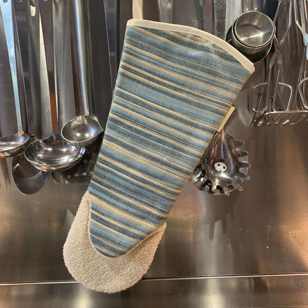 long gauntlet style oven glove with blue stripes hanging along with stainless steel utensils