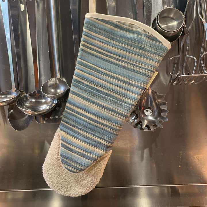 long gauntlet style oven glove with blue stripes hanging along with stainless steel utensils