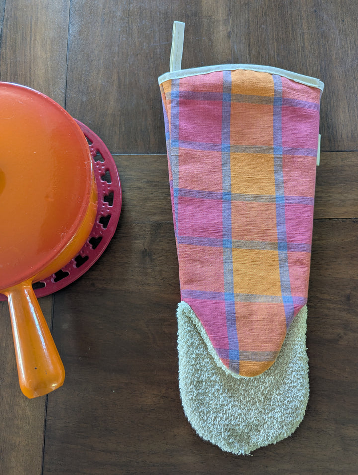 Plaid oven mitt orange pink and blue on a wooden surface with a colourful le creuset dish in the background