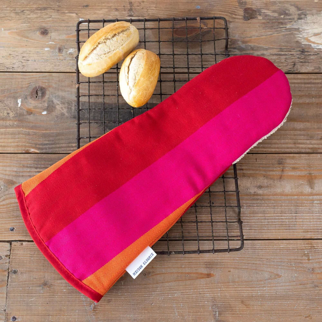 elegant looking long oven glove red and pink on a wooden support with 2 small breads