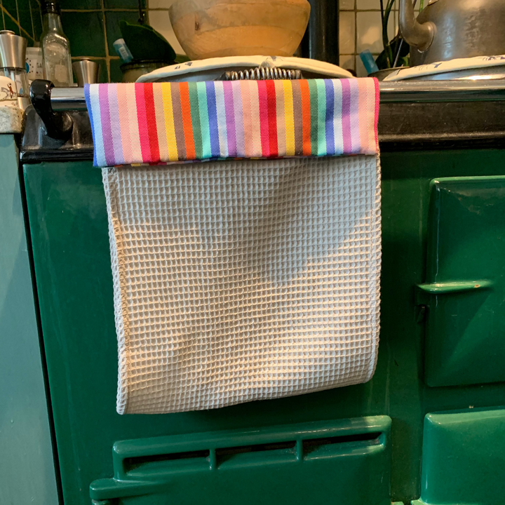 Hand towel Roller towel with rainbow header and beige cotton waffle fabric hanging over a green Aga range cooker front railing 