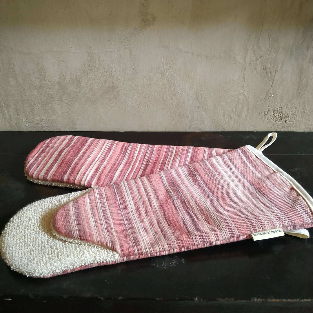 a pair of gauntlet oven gloves red striped on a black side board with a beige backdrop