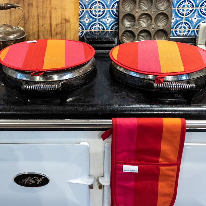 A pair of  red, pink  and orange striped hob covers  on a a baby blue Aga stove with a blue patterned backsplash, and a matching oven glove