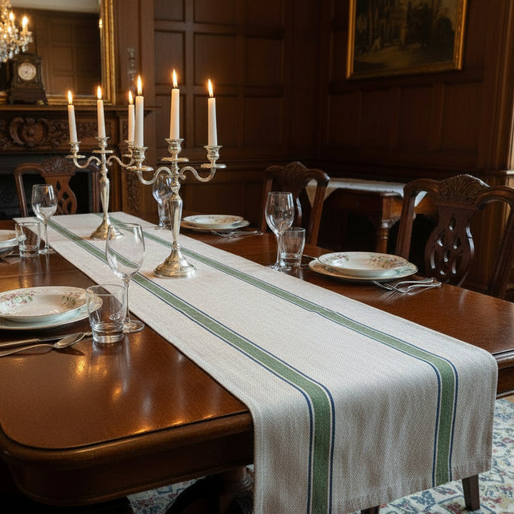 Dining table set for a meal with candles, plates, and a striped blue and green with a linen base runner in a formal dining room.
