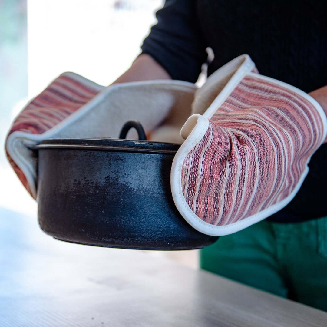 person with red double oven mitts holding a cast iron pot