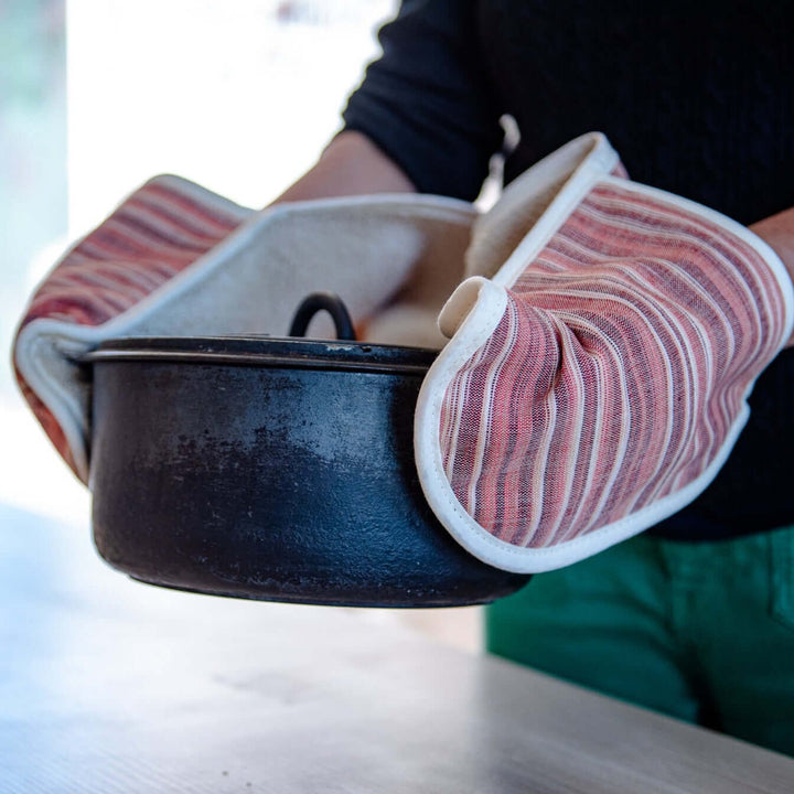 person with red double oven mitts holding a cast iron pot