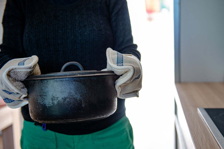 person in background with oven gloves holding a black pot 