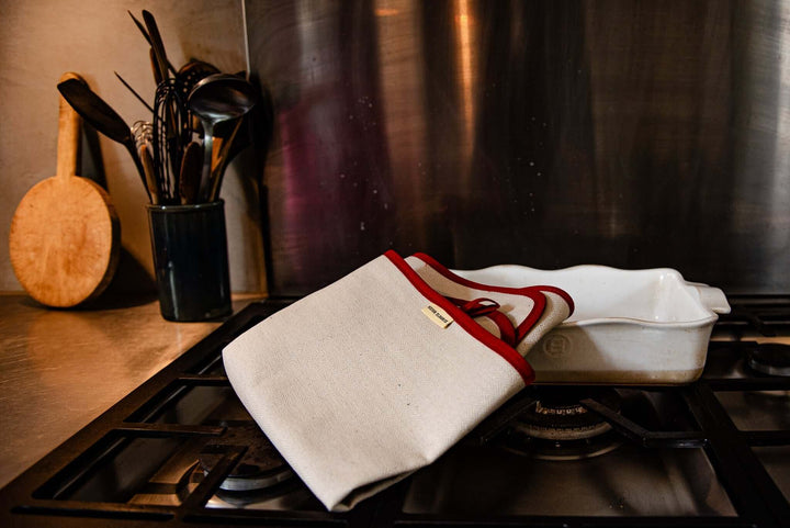 oven cloth natural with red bias folded over a white serving dish with a dark kitchen background