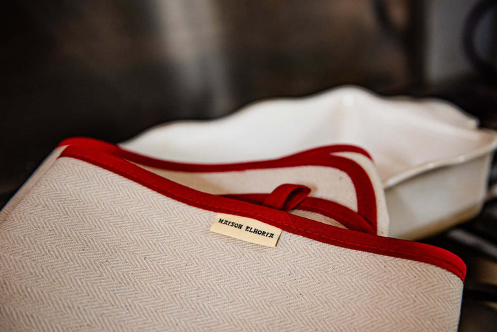 Part of an oven cloth natural with red bias folded over a white oven dish 