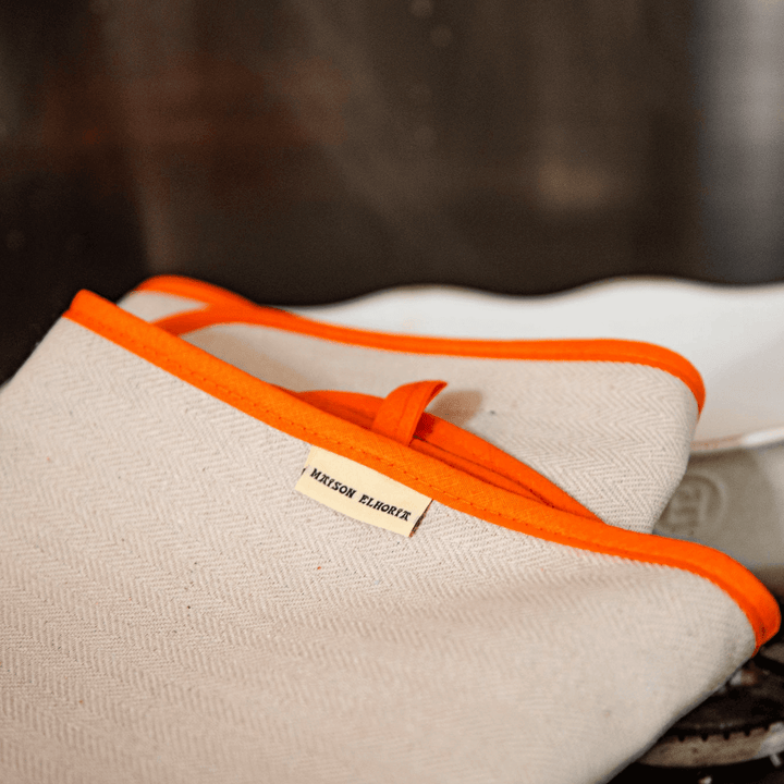oven cloth with orange bias  close up on a cooker, resting on a white oven dish