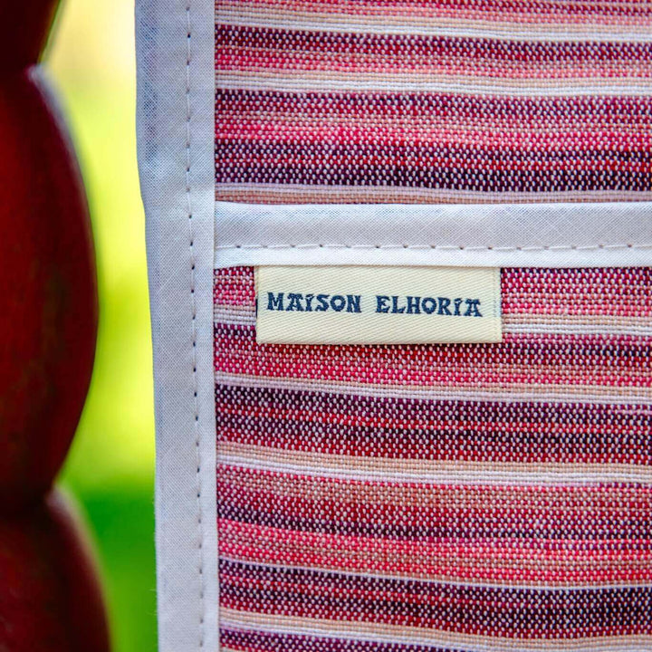 close up of a small part of a red striped double oven glove with its Maison Elhoria brand label hanging vertically