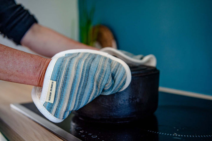 close up over a person arms holding a cast iron pot with a blue stripes pot holder