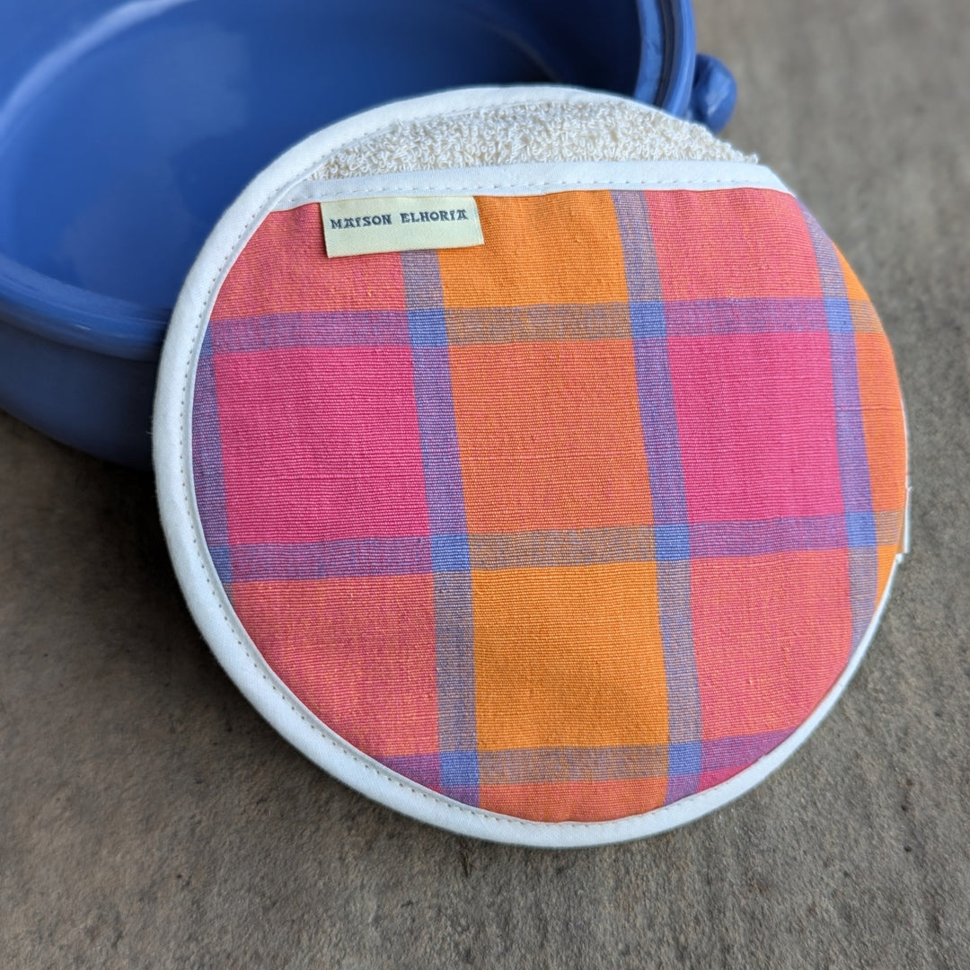 Round colourful fabric item with a blue earth ware cooking pot in the background