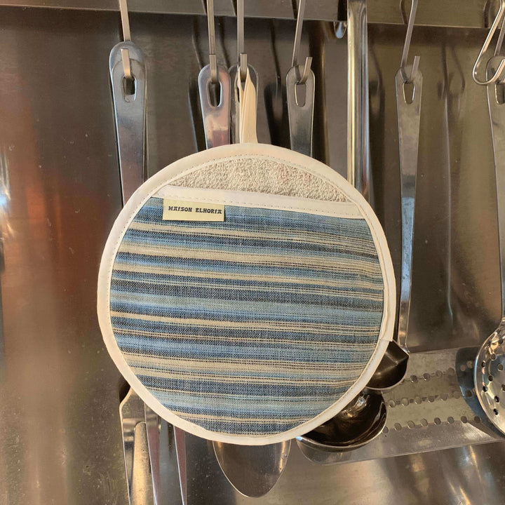 Pot grabber round with textured blue stripes hanging with stainless steel kitchen tools
