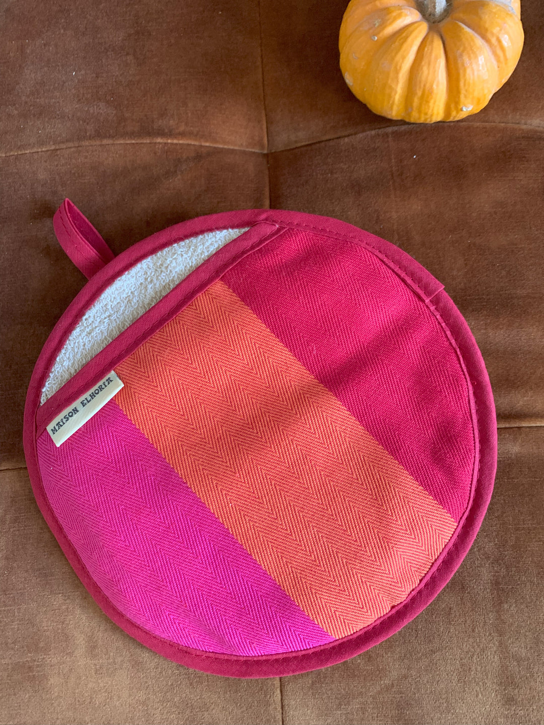 Pink and orange checkered pot holder on a brown surface with a small yellow pumpkin.