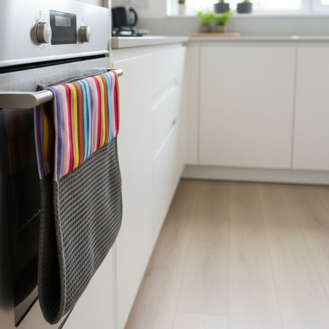 Gray waffle cotton hand towel roller shaped with a rainbow striped fabric header rolled over a metallic oven handle in a modern kitchen