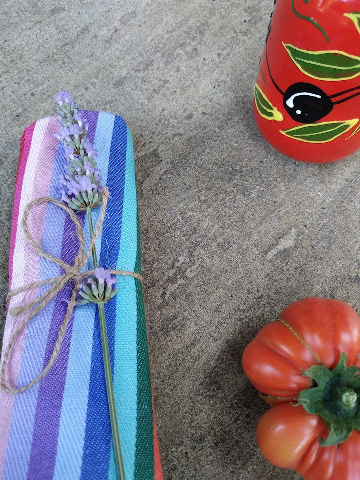 Colorful striped fabric with twine and lavender on a concrete surface, with red peppers in the foreground.