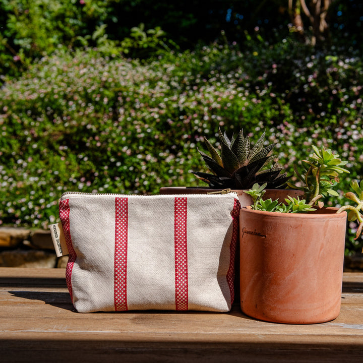 Fabric pouch with red stripes on a wooden surface with plants in the background