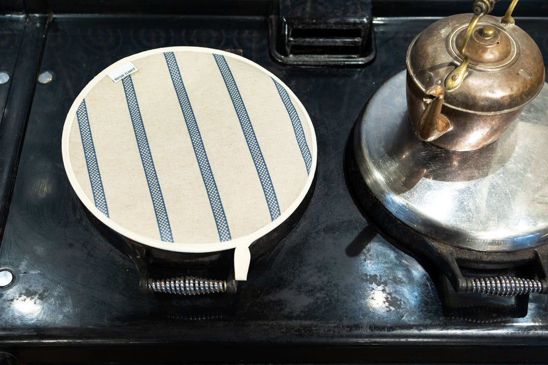 Chef pad linen union with blue stripes displayed on top of an Aga hob lid cover with an antique kettle on the side