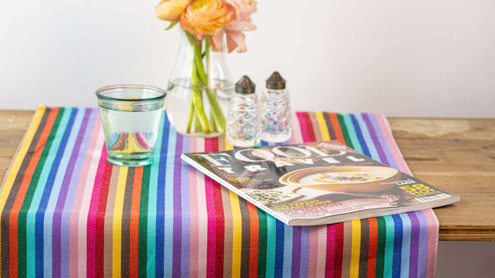 Bright and cheerful side board setting with a rainbow-striped table runner, napkins to match, and a vase elegantly placed at the center