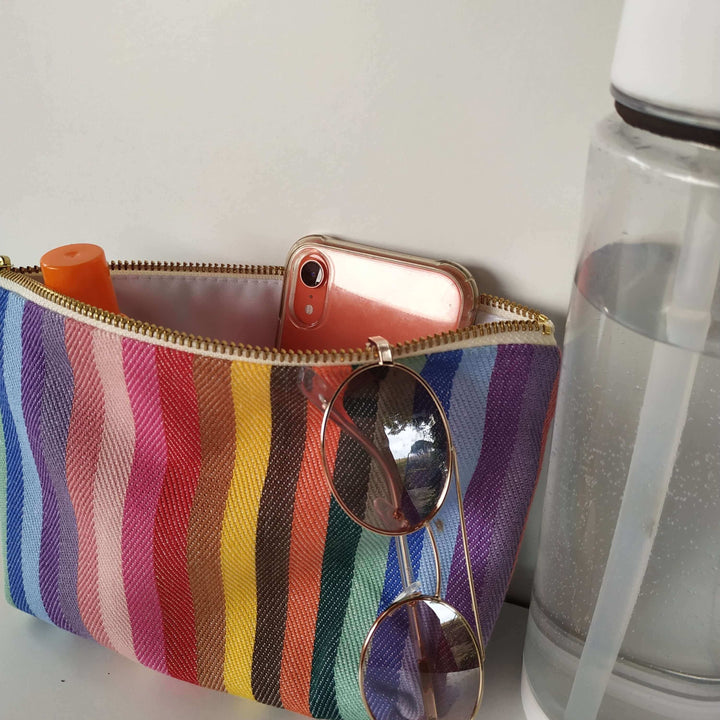 rainbow wash bag open showing sun cream , sunglasses and a clear water bottle on the right hand side