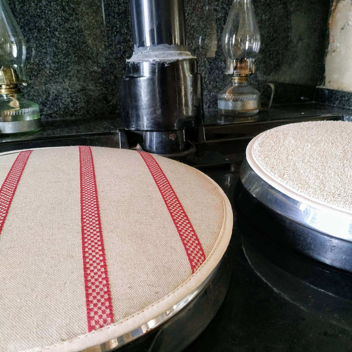 Two Linen union with Red stripes insulating Aga hob plate cover on Aga with 2 petrol lamps in the background.. Products image cut on either side