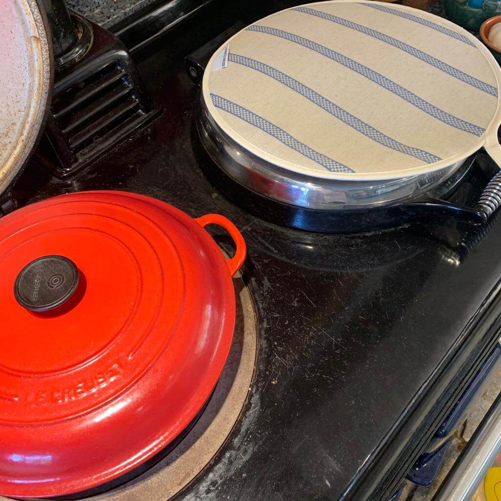 Linen union with blue stripes insulating Aga hob plate cover on Aga with Red cast iron pot next to it