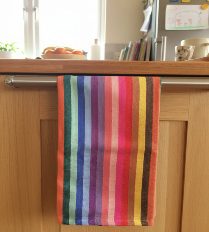 rainbow kitchen towel hanging over an wooden kitchen cupboard  metal railing with a window in the background